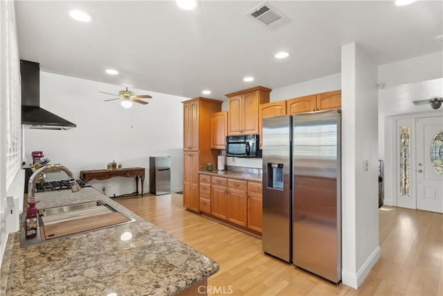 kitchen featuring visible vents, stainless steel fridge with ice dispenser, wall chimney range hood, black microwave, and a sink