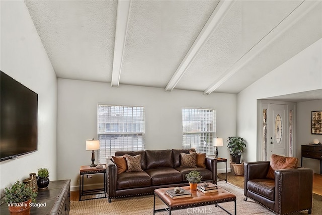 living room with vaulted ceiling with beams, a textured ceiling, and baseboards