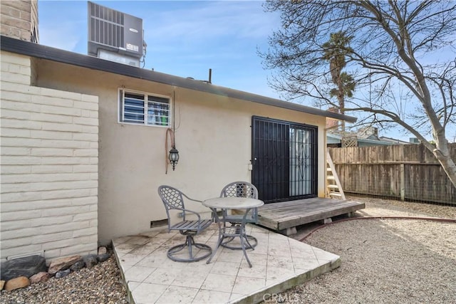 view of exterior entry with a patio, central AC unit, fence, and stucco siding