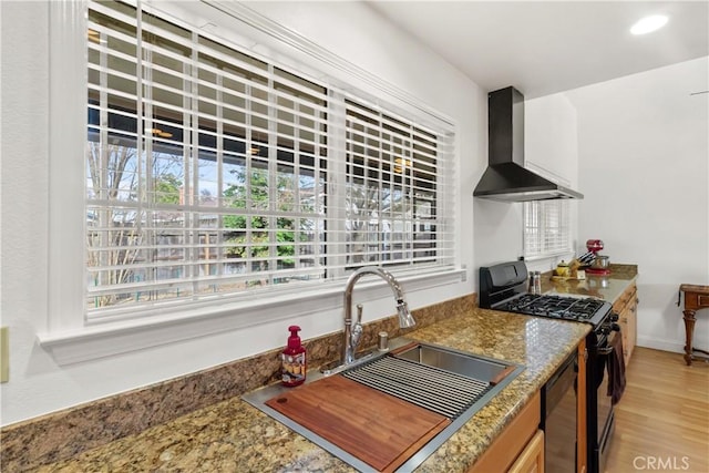 kitchen featuring black gas range oven, light wood-type flooring, wall chimney range hood, a sink, and recessed lighting