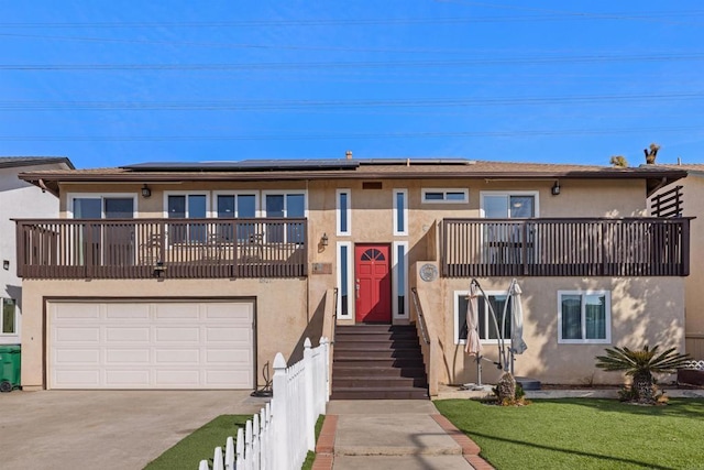 multi unit property featuring driveway, a balcony, fence, roof mounted solar panels, and stucco siding