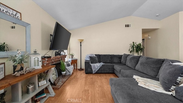 living room featuring lofted ceiling, a brick fireplace, visible vents, and light wood-style flooring