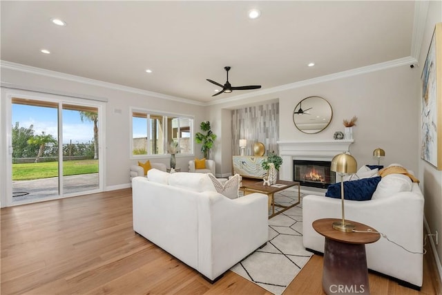 living room featuring a glass covered fireplace, recessed lighting, light wood-style floors, and ornamental molding