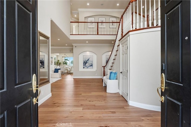 entrance foyer featuring baseboards, light wood finished floors, stairs, a towering ceiling, and crown molding