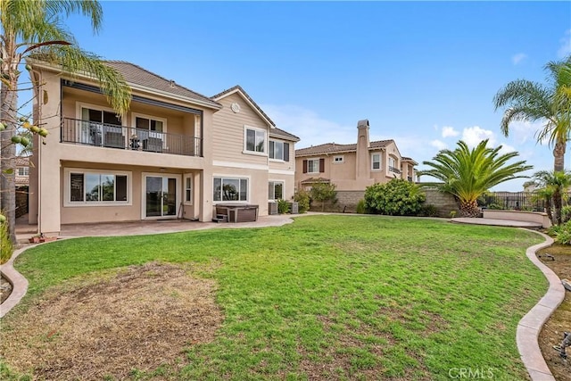 rear view of property with stucco siding, a patio, fence, a yard, and a balcony