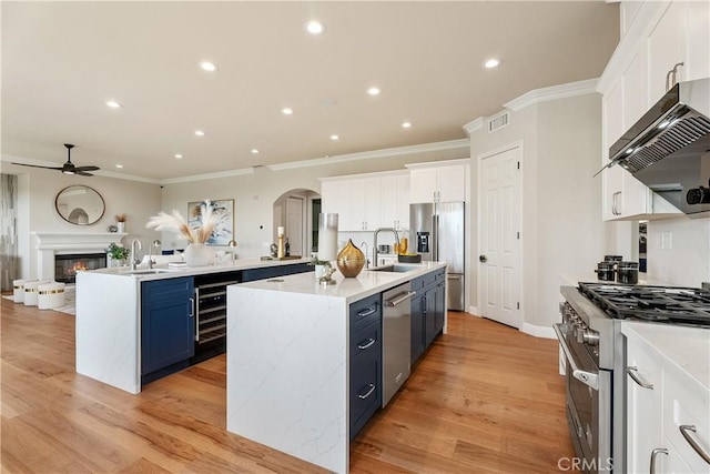 kitchen with visible vents, wall chimney range hood, wine cooler, a center island with sink, and stainless steel appliances