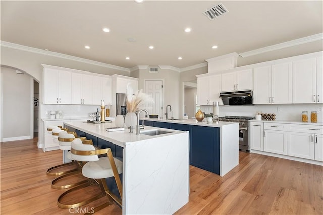 kitchen featuring visible vents, a kitchen island with sink, a sink, stainless steel appliances, and arched walkways