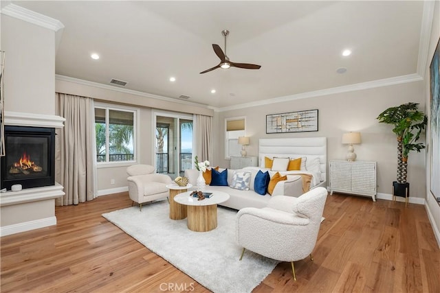 living area with visible vents, baseboards, light wood-style floors, a glass covered fireplace, and crown molding