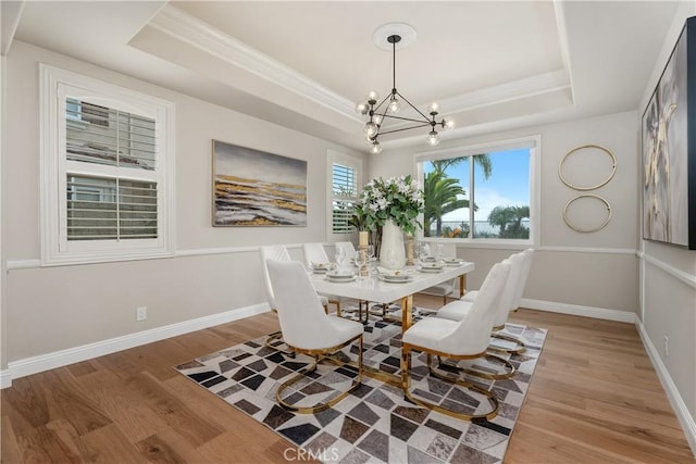 dining space with a notable chandelier, a raised ceiling, baseboards, and wood finished floors