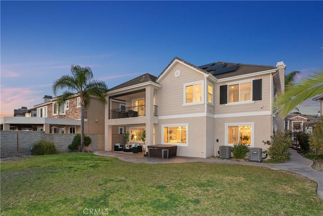 back of property with a patio, a balcony, central AC unit, solar panels, and a yard