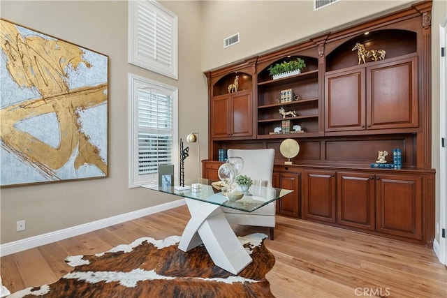 office with a high ceiling, light wood-style floors, visible vents, and baseboards