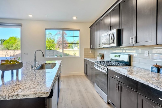 kitchen featuring appliances with stainless steel finishes, a sink, decorative backsplash, and light stone countertops