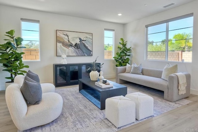 living area with baseboards, wood finished floors, visible vents, and a healthy amount of sunlight