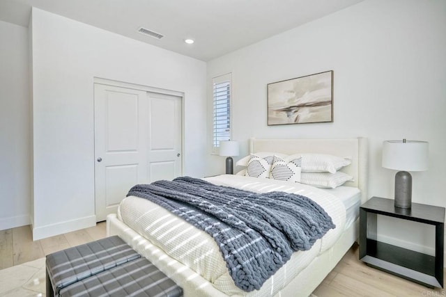 bedroom with light wood-style floors, baseboards, visible vents, and a closet