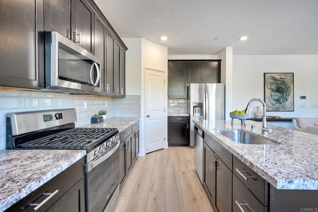 kitchen with light wood finished floors, appliances with stainless steel finishes, a sink, light stone countertops, and backsplash