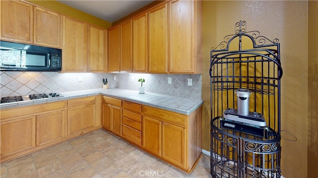 kitchen featuring black microwave, tile countertops, backsplash, and stainless steel gas cooktop