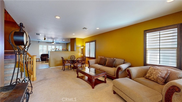 living room with a wealth of natural light, light colored carpet, visible vents, and stairs