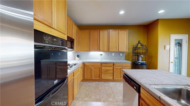 kitchen featuring tasteful backsplash, tile countertops, black appliances, a sink, and recessed lighting