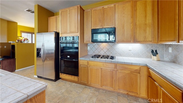 kitchen featuring visible vents, black appliances, tasteful backsplash, and tile counters