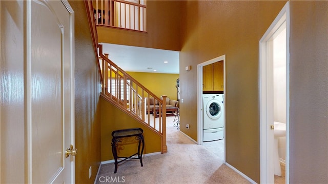 hall featuring light carpet, washer / dryer, baseboards, and stairway