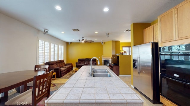 kitchen with dobule oven black, stainless steel fridge, tile counters, open floor plan, and light brown cabinets