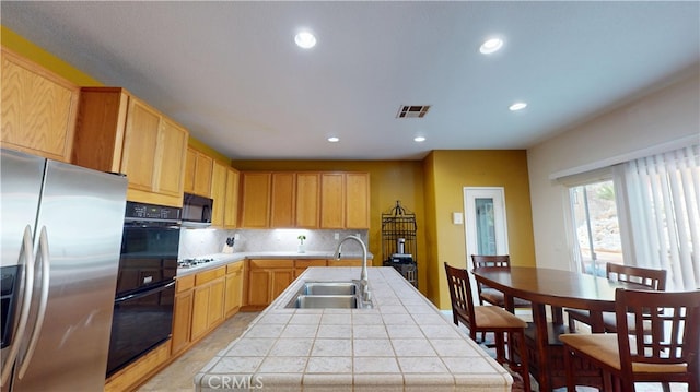 kitchen featuring tile countertops, black microwave, a sink, visible vents, and stainless steel refrigerator with ice dispenser