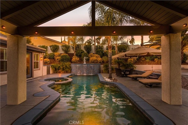 pool at dusk with a pool with connected hot tub and a patio