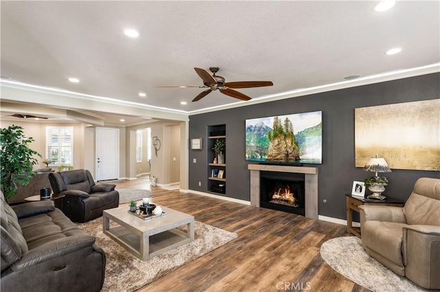 living room with a warm lit fireplace, ornamental molding, wood finished floors, and recessed lighting