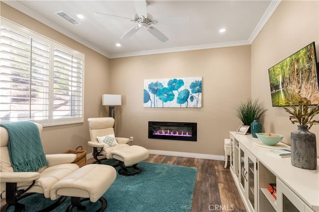 living area with dark wood-style floors, crown molding, visible vents, a glass covered fireplace, and baseboards