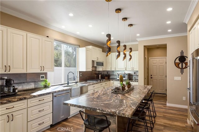 kitchen featuring dark wood-style floors, appliances with stainless steel finishes, ornamental molding, a sink, and a kitchen breakfast bar