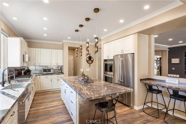 kitchen with stainless steel appliances, a kitchen breakfast bar, ornamental molding, dark stone countertops, and dark wood finished floors