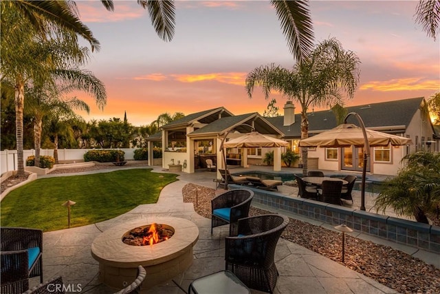 back of house featuring a hot tub, a fire pit, a lawn, a patio, and a fenced backyard