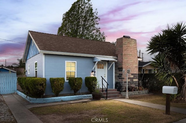 view of front of property with entry steps, a shingled roof, a chimney, and fence