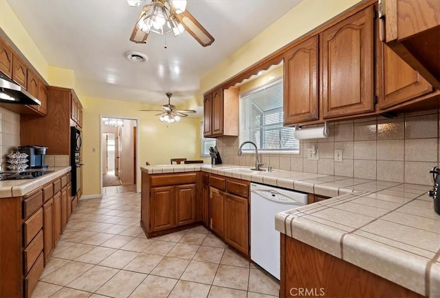 kitchen featuring tile countertops, white dishwasher, brown cabinetry, and a peninsula