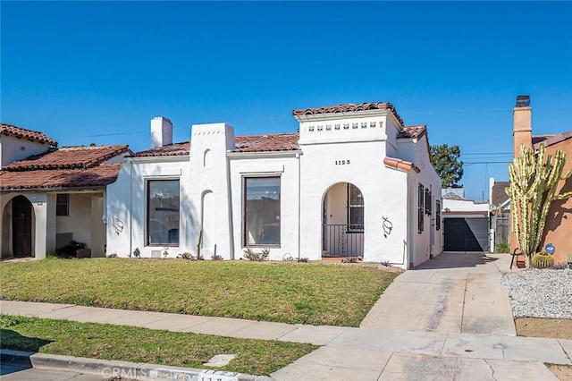 mediterranean / spanish-style house with driveway, a tiled roof, a front lawn, and stucco siding