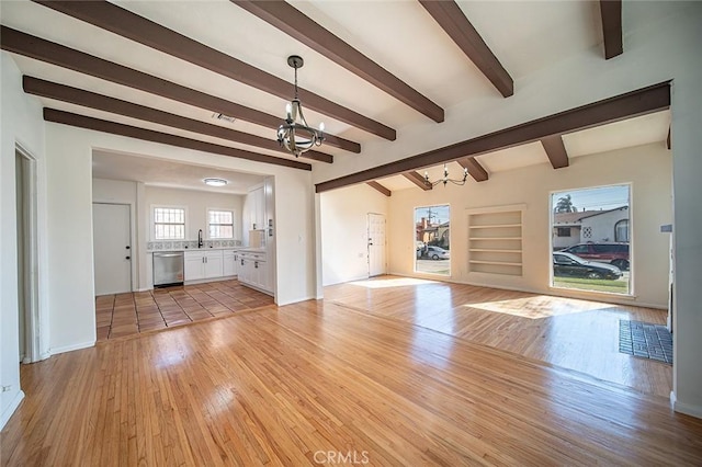 unfurnished living room featuring a sink, light wood finished floors, beam ceiling, and a notable chandelier