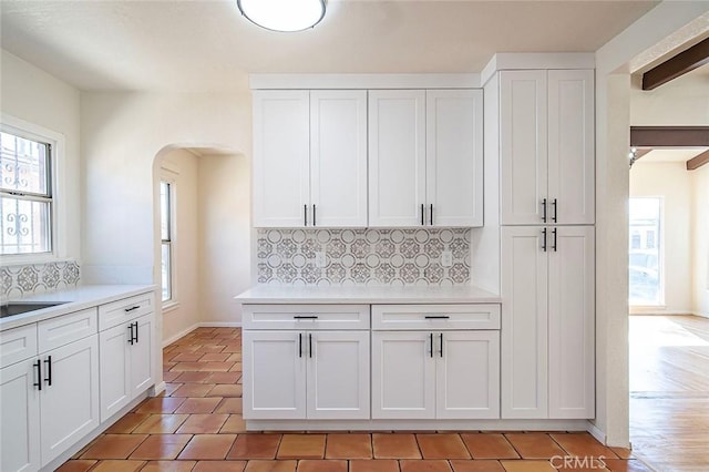 kitchen with arched walkways, white cabinets, light countertops, and decorative backsplash