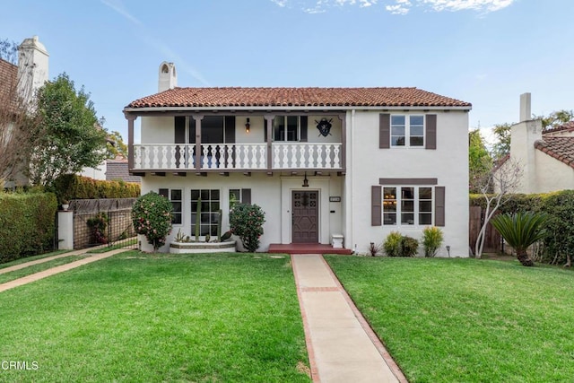 mediterranean / spanish home featuring a balcony, fence, stucco siding, a front lawn, and a chimney