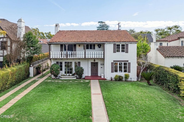 mediterranean / spanish home with a fenced backyard, a balcony, a tile roof, a chimney, and a front yard