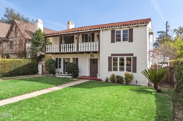 mediterranean / spanish-style house with a front yard, fence, a balcony, and stucco siding