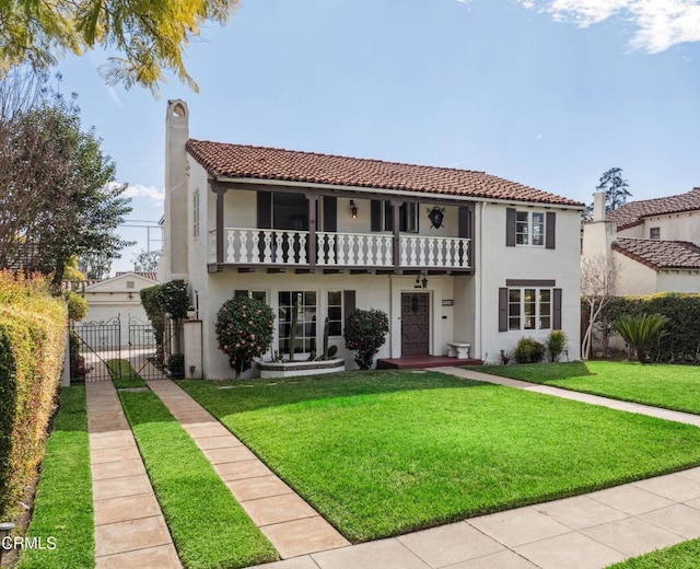 mediterranean / spanish house with a balcony, a chimney, fence, a front yard, and stucco siding