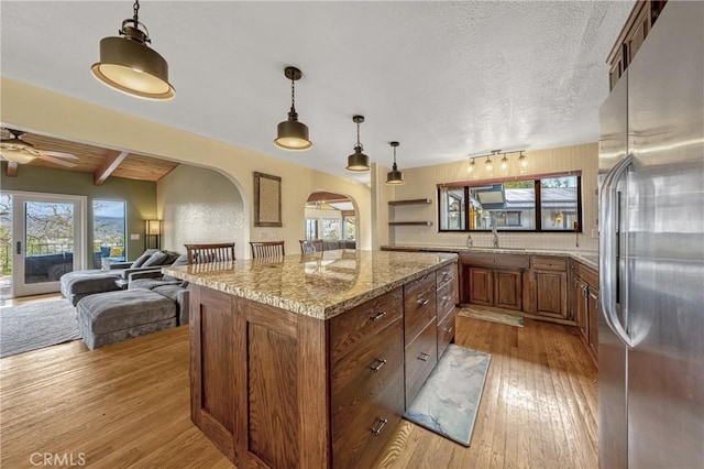 18945 Timber Point Rd, Hidden Valley Lake, CA 95467 - kitchen featuring brown cabinets, a center island, arched walkways, light wood-type flooring, and stainless steel refrigerator