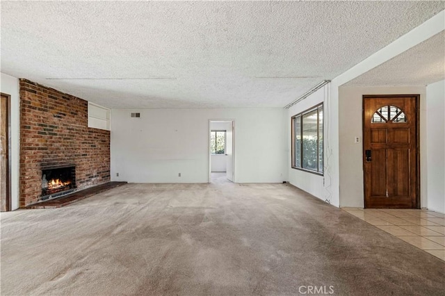 unfurnished living room with light carpet, light tile patterned floors, visible vents, a textured ceiling, and a brick fireplace