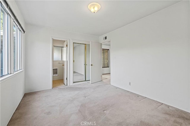 unfurnished bedroom featuring visible vents, ensuite bathroom, a closet, and light colored carpet