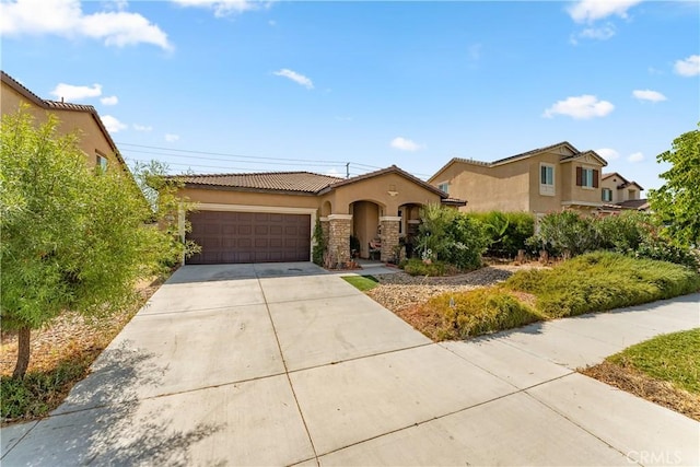 mediterranean / spanish home with an attached garage, driveway, a tiled roof, and stucco siding