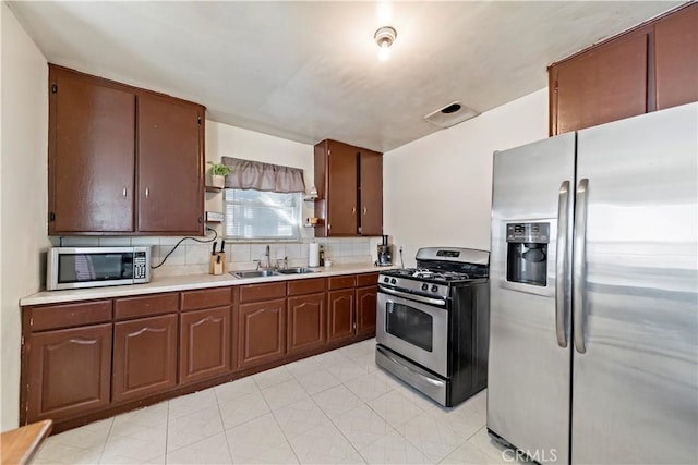 kitchen featuring tasteful backsplash, appliances with stainless steel finishes, light countertops, open shelves, and a sink