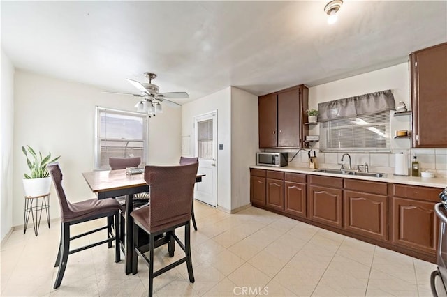 kitchen with open shelves, tasteful backsplash, light countertops, stainless steel microwave, and a sink