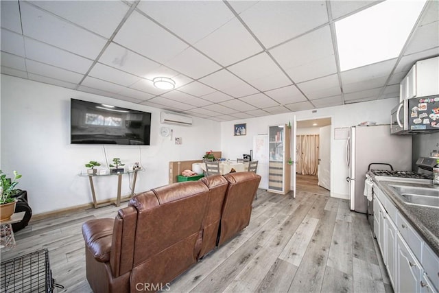 living area with a paneled ceiling, light wood-style flooring, and a wall mounted AC