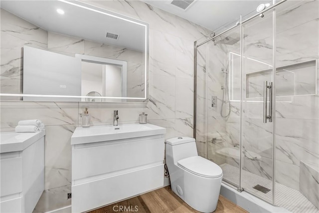 bathroom with a marble finish shower, visible vents, toilet, vanity, and wood finished floors