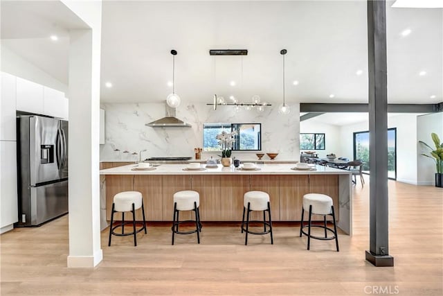 kitchen featuring modern cabinets, a breakfast bar, wall chimney range hood, white cabinetry, and stainless steel refrigerator with ice dispenser